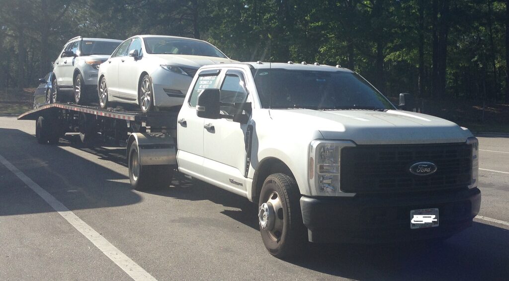 White pickup tow truck hauling a car on a flatbed trailer